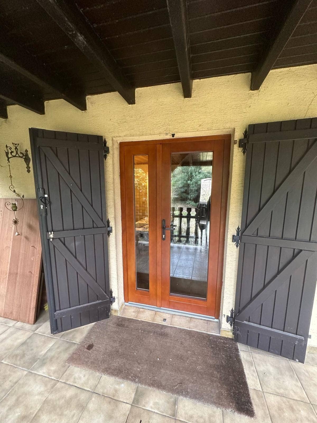 Porte-fenêtre en bois ton acajou vitrée sous auvent, encadrée de volets bois, posée par REM Fermetures