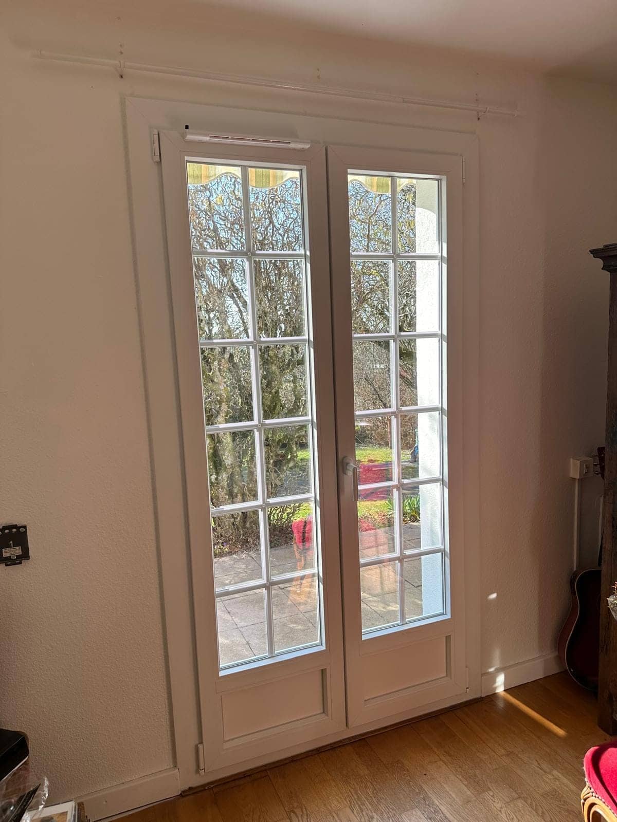 Porte-fenêtre PVC blanche à petits-bois ouvrant sur le jardin, posée par REM Fermetures