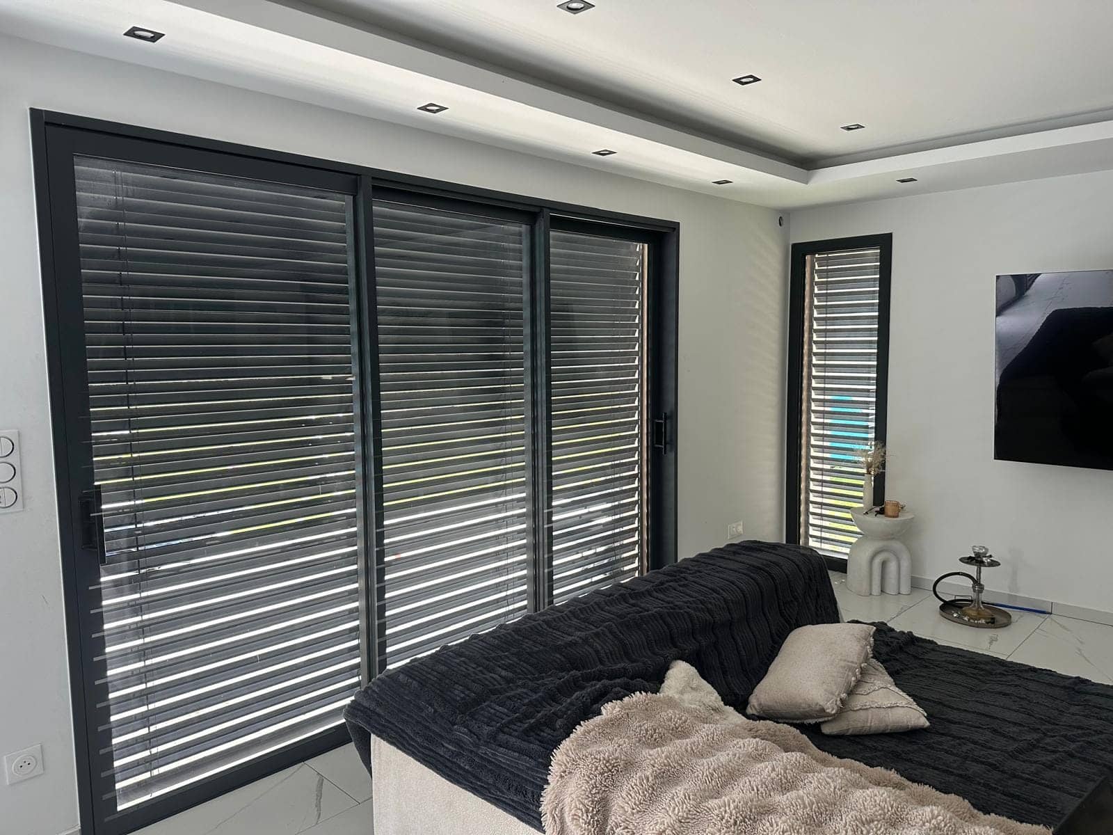 Brise-soleil orientables en aluminium sur les baies vitrées d'une chambre contemporaine, posés par REM Fermetures
