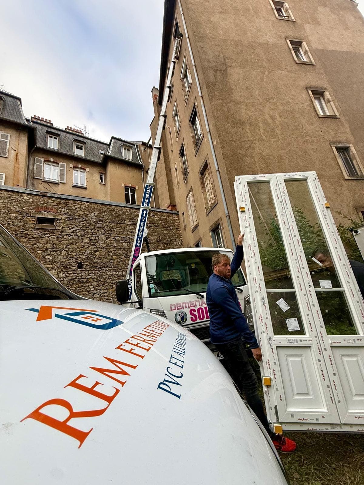 Artisan de REM Fermetures manipulant une menuiserie PVC près du camion floqué de l'entreprise à Belfort