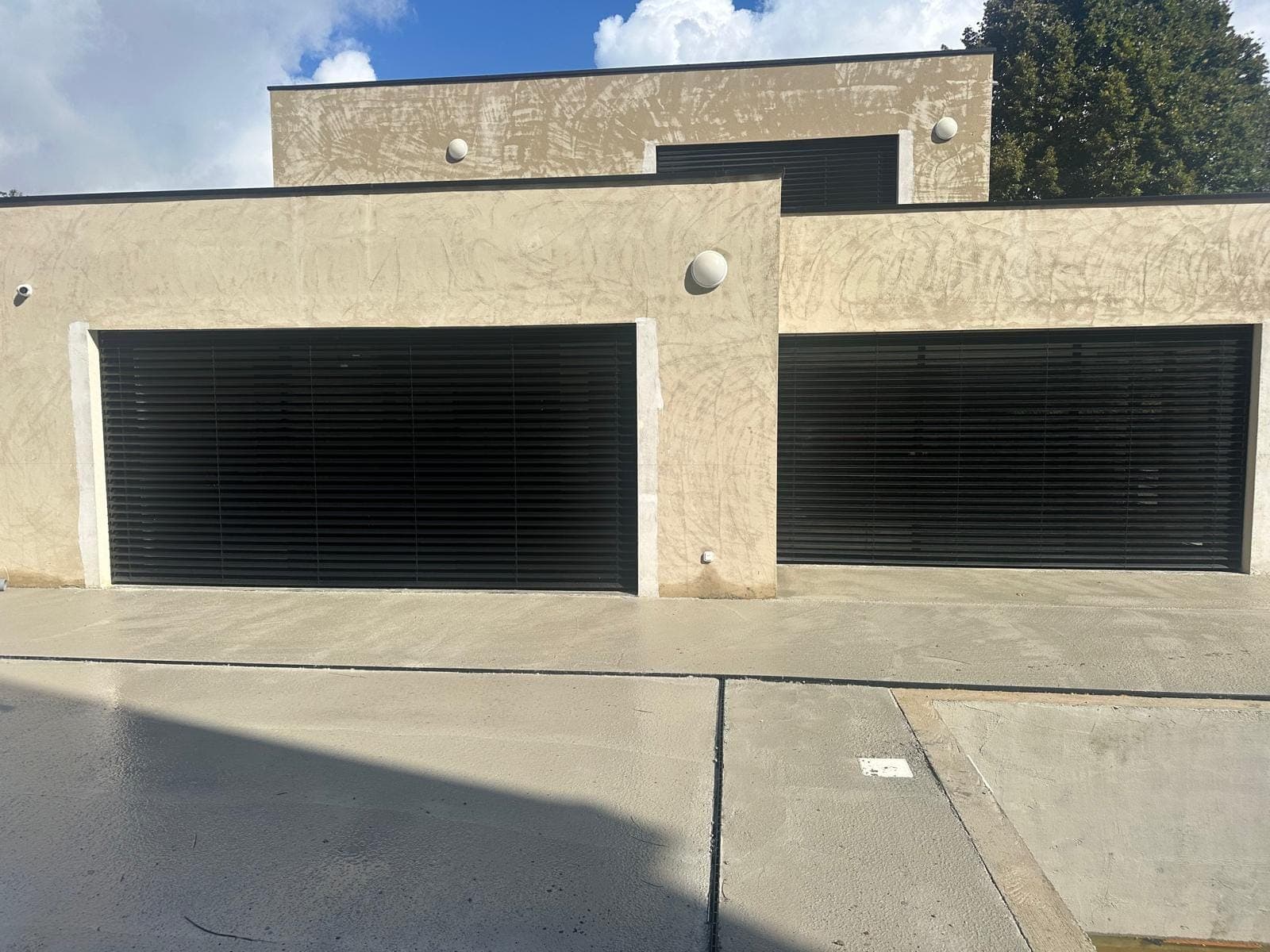 Deux portes de garage à lames noires sur une villa contemporaine au crépi clair, réalisées par REM Fermetures