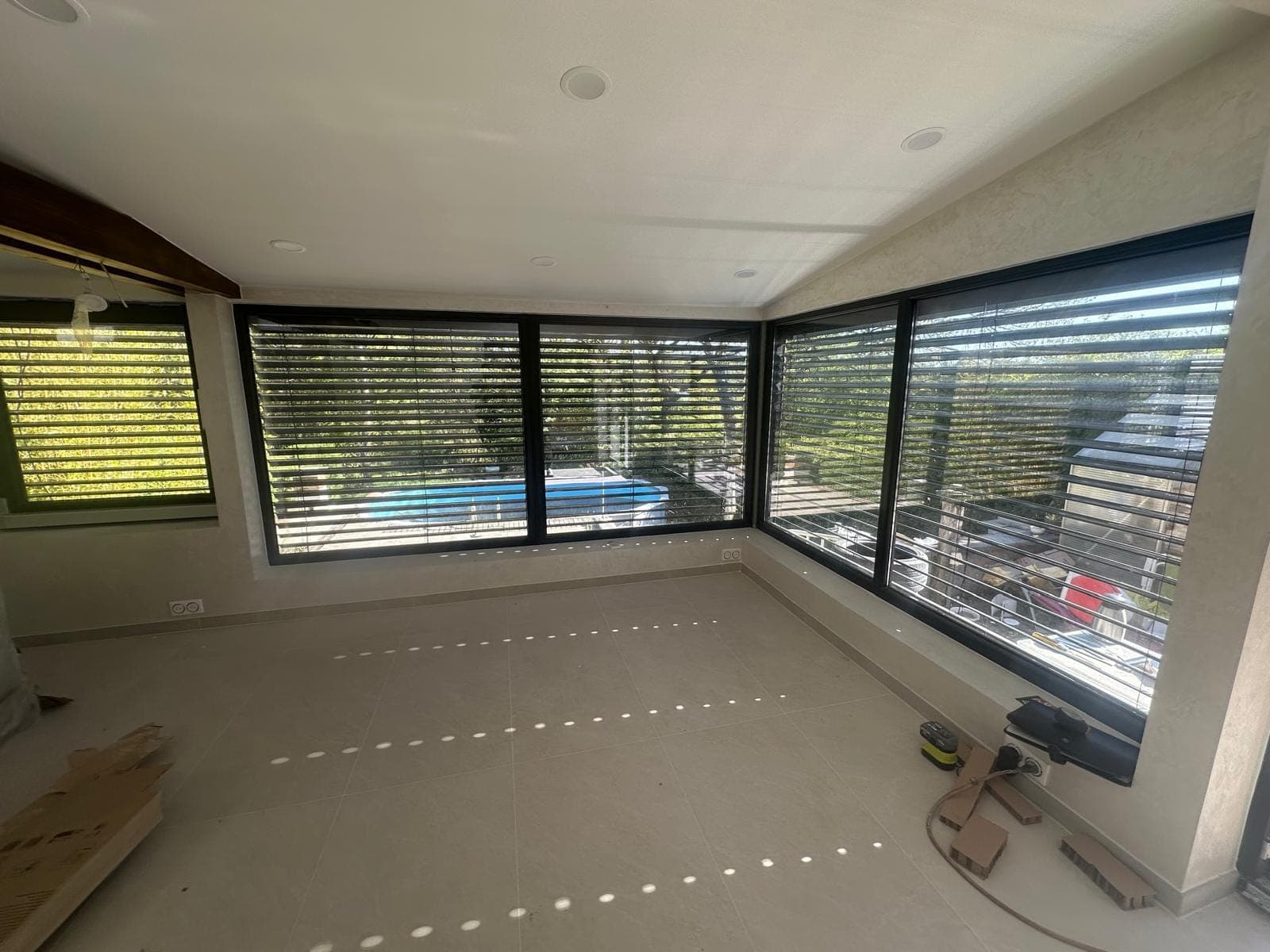 Pièce d'angle avec baies vitrées et brise-soleil orientables donnant sur la piscine, par REM Fermetures