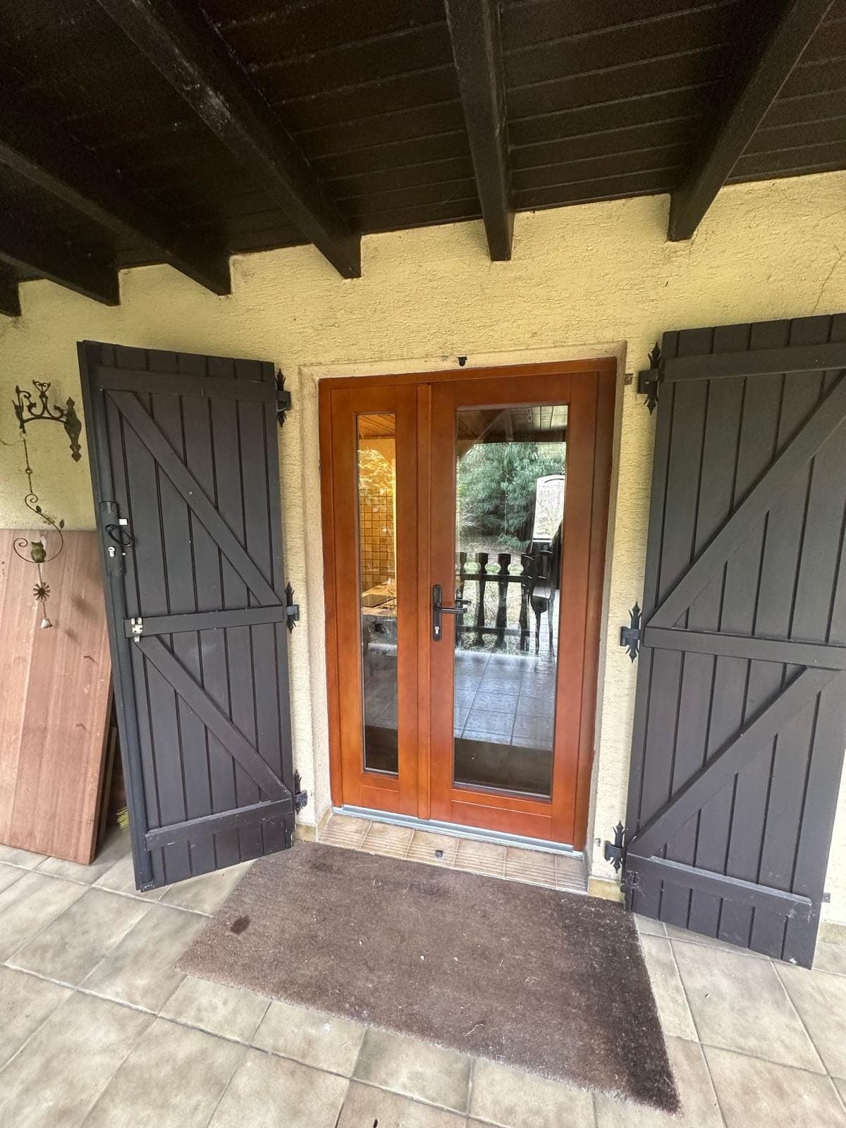 Porte-fenêtre en bois ton acajou vitrée sous auvent, encadrée de volets bois, posée par REM Fermetures