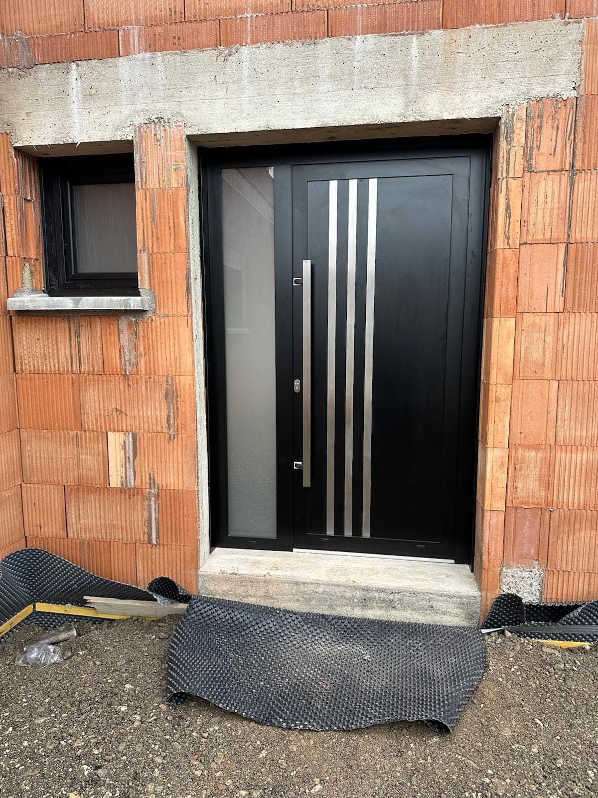 Porte d'entrée en aluminium noir au design contemporain avec poignée inox, installée par REM Fermetures