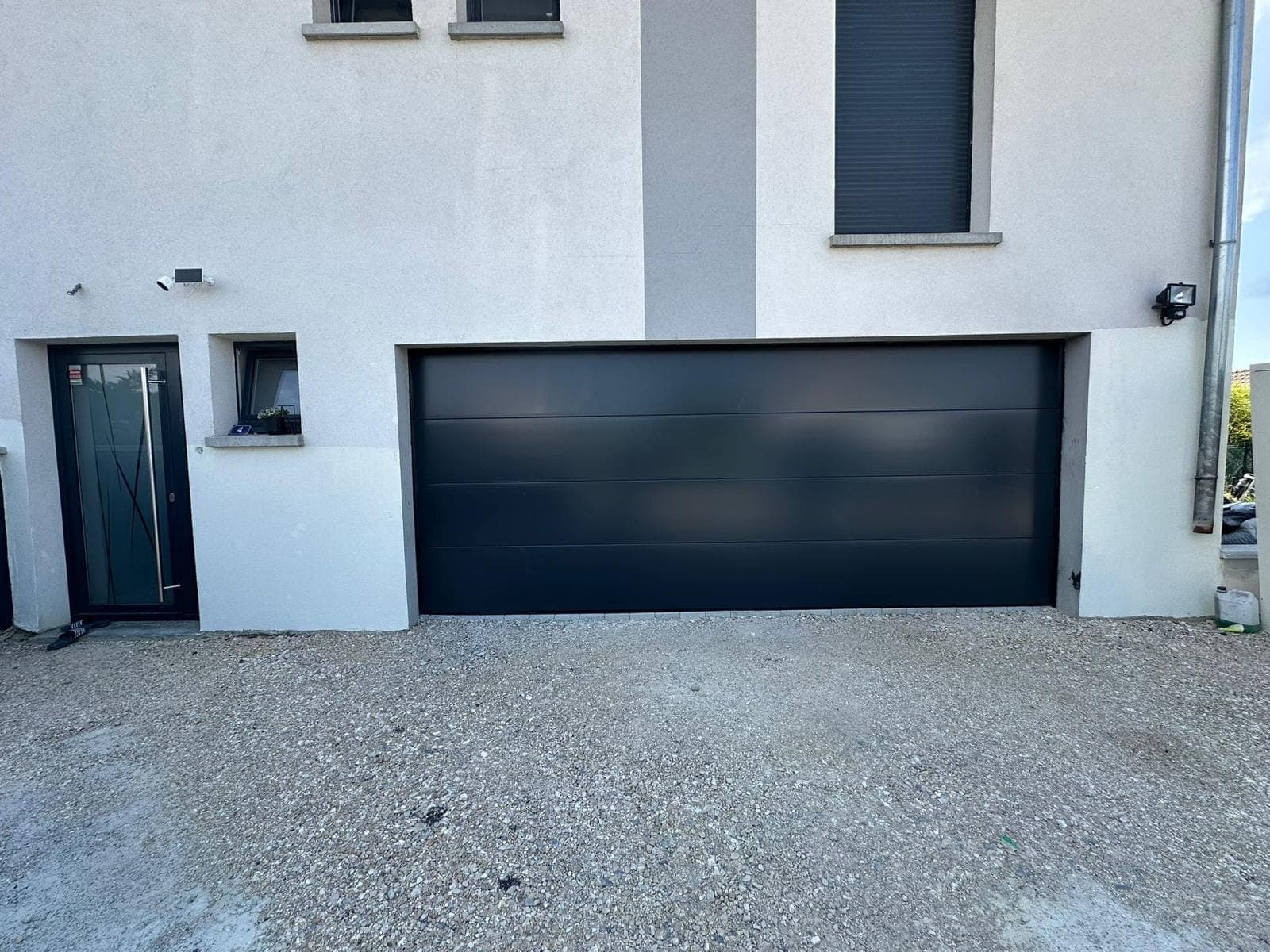 Porte de garage sectionnelle anthracite et porte de service assortie sur façade claire, installées par REM Fermetures
